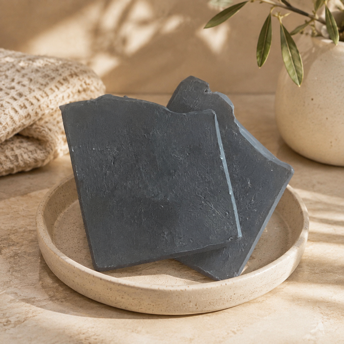 Two Activated Charcoal handmade soap bars styled on a wooden board in a warm neutral setting